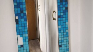 A mirror with a blue mosaic frame reflecting a hallway with a wooden door and a white wall. - Small Cozy Room in Chelmsford Springfield (Springfield)