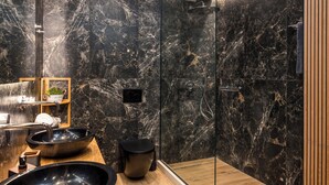 A modern bathroom with a black marble wall, a wooden vanity, a black sink, and a glass shower enclosure. - Aithra Seaview Suite by Konnect (Barbati)