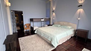 Een slaapkamer met een stapelbed, een eenpersoonsbed, een stoel, een nachtkastje en een klein kastje.