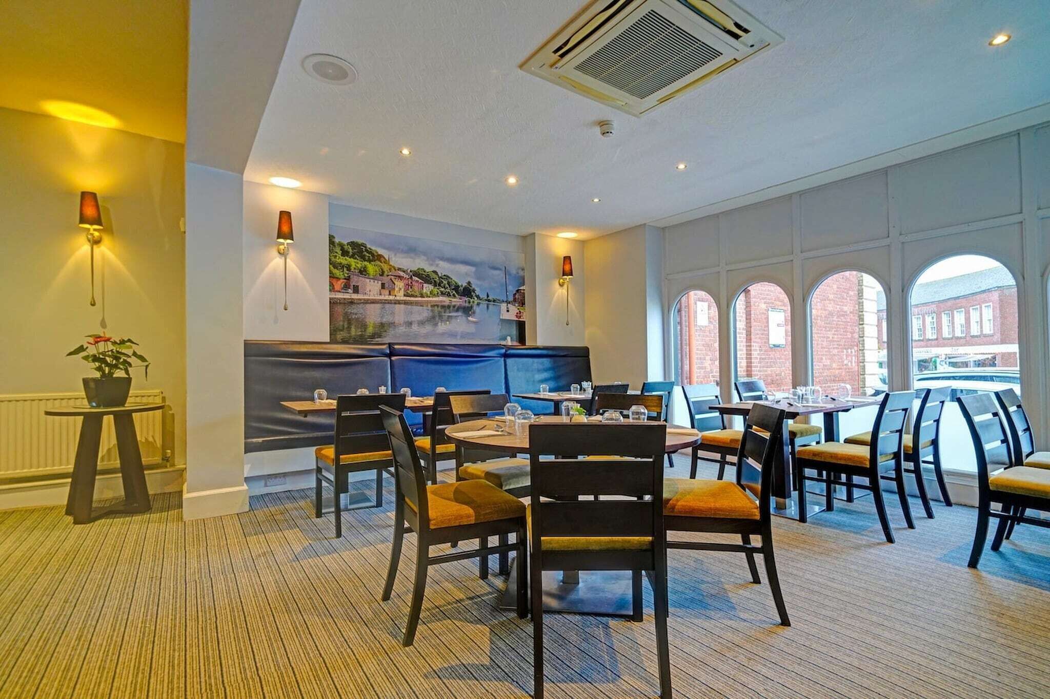 A dining area with round tables and chairs, a mural on the wall, and large windows with a view of buildings.