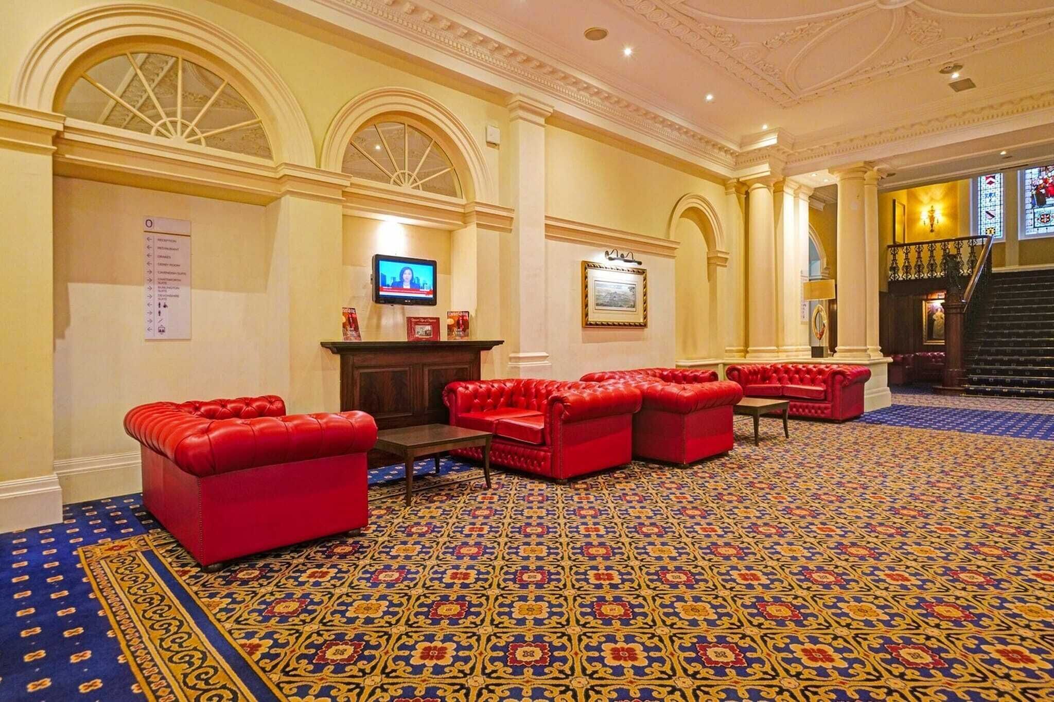 A lobby with red leather sofas, a patterned carpet, and a staircase.