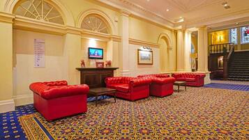A lobby with red leather sofas, a patterned carpet, and a staircase.
