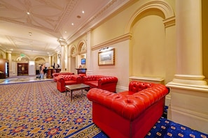 Eine Hotelhalle mit roten Ledersofas, einem gemusterten Teppich und klassischer Architektur.