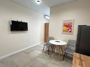Una habitación moderna con televisión de pantalla plana, refrigerador, una mesa de comedor con sillas y un cartel en la pared.