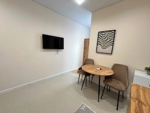 Una habitación moderna con una televisión de pantalla plana montada en la pared, una mesa redonda de madera con cuatro sillas y una obra de arte enmarcada sobre la mesa.