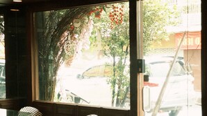 A restaurant with a large window, wooden furniture, and a view of the street outside. - Room with a Temple View (Phra Nakhon)