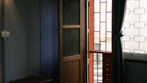 A room with a wooden door, a small bedside table, and a window with a view of buildings. - Room with a Temple View (Phra Nakhon)