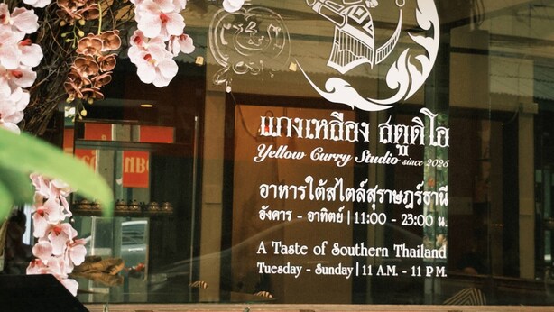 A restaurant window with Thai script and a logo, surrounded by pink orchids. - Room with a Temple View (Phra Nakhon)