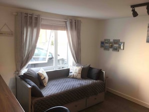 A small, cozy room with a bed, a window with curtains, a radiator, and a wall with framed pictures.