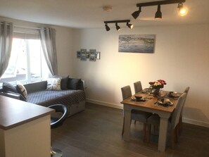 Et værelse med en seng, et spisebord med stole, et vindue med gardiner og et billede på væggen.