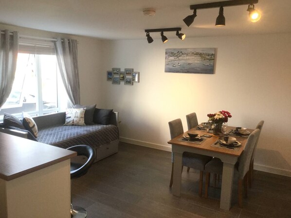 Une pièce comprenant un lit, une table à manger avec des chaises, une fenêtre avec des rideaux et un tableau accroché au mur.