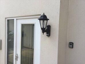 En dør med et glasfelt, en sort vægmonteret lampe og en lille el-installation på væggen.