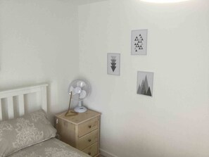 Et soveværelse med en seng, et natbord med en ventilator og tre billeder på væggen.