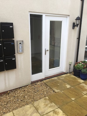 A white door with a glass panel, a wall-mounted electrical box, and potted plants.