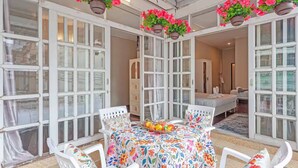 A room with a dining table, chairs, hanging flower baskets, and a bed.