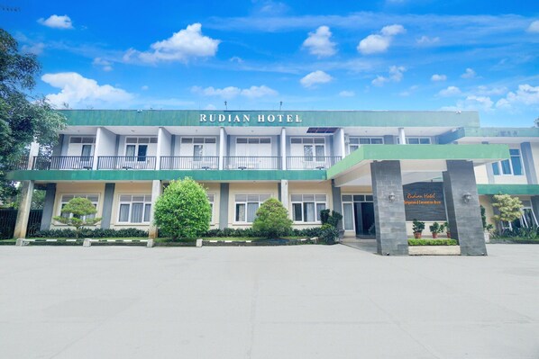 A hotel with a green and white facade, named 'RUDIAN HOTEL,' featuring a covered entrance and a landscaped front yard. - Luxury Family Suite W/ Free Wifi Parking and Pool (Cisarua)