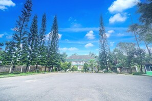 A spacious paved area with tall trees and a building with a green roof. - Luxury Family Suite W/ Free Wifi Parking and Pool (Cisarua)