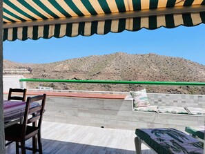 Una terraza con vistas a un paisaje montañoso, una mesa con sillas y una cama con colcha estampada.