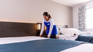 A hotel room with a neatly made bed, a bedside table with a lamp, and a window with patterned curtains. - 2 Full Beds | Non-Smoking (Grants)