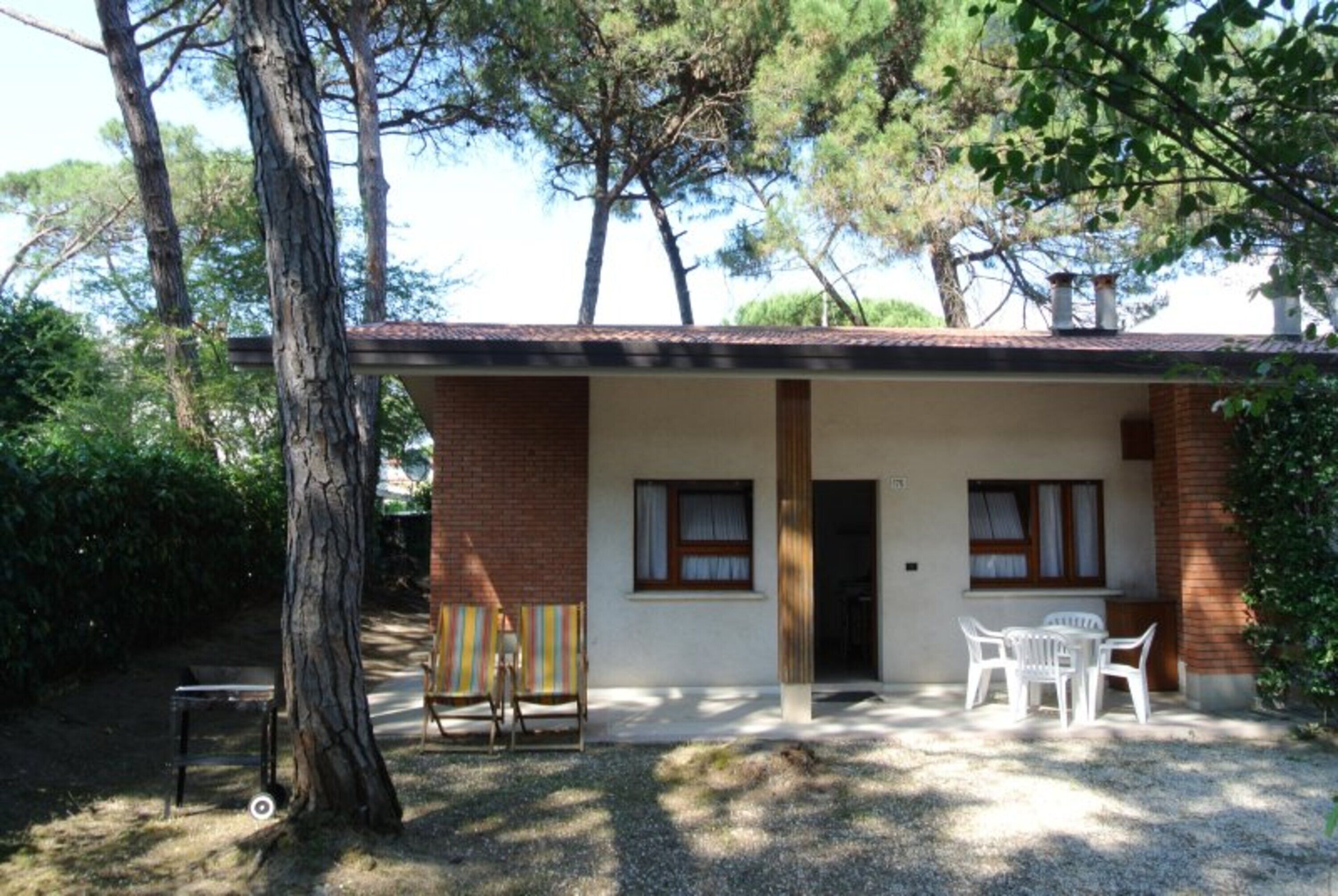 Ein kleines Gebäude mit Ziegelaußenwand, zwei Fenstern, einer Tür und einer Terrasse mit Tisch und Stühlen.