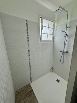Un baño con ducha, ventana y retrete.
