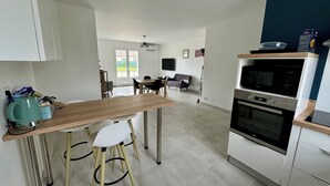 Eine moderne Küche mit einem Holztisch, weißen Stühlen, einem eingebauten Backofen und einem an der Wand montierten Fernseher.