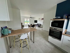 Una cocina moderna con una mesa de comedor de madera, sillas blancas, horno empotrado y televisor montado en la pared.