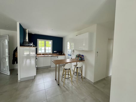 A modern kitchen with white cabinets, a wooden dining table, and two stools.