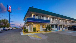 Um motel com uma placa de 'WELCOME', um estacionamento e um céu claro.