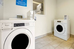 Une buanderie équipée de deux lave-linge Whirlpool, un panneau indiquant que le motel n’est pas responsable des objets laissés sans surveillance, et une petite fenêtre.