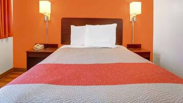 Quarto de hotel com uma cama, duas luminárias de cabeceira, uma mesa de apoio com telefone e uma parede laranja.