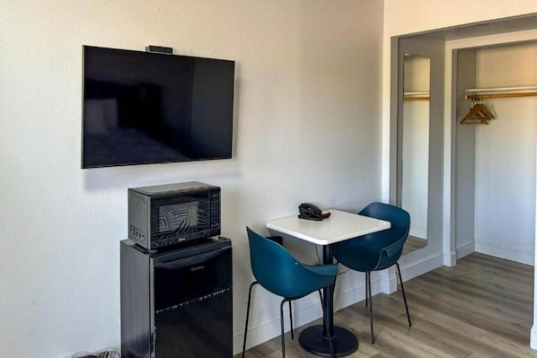 Una habitación pequeña con televisión, microondas, una mesa y dos sillas.
