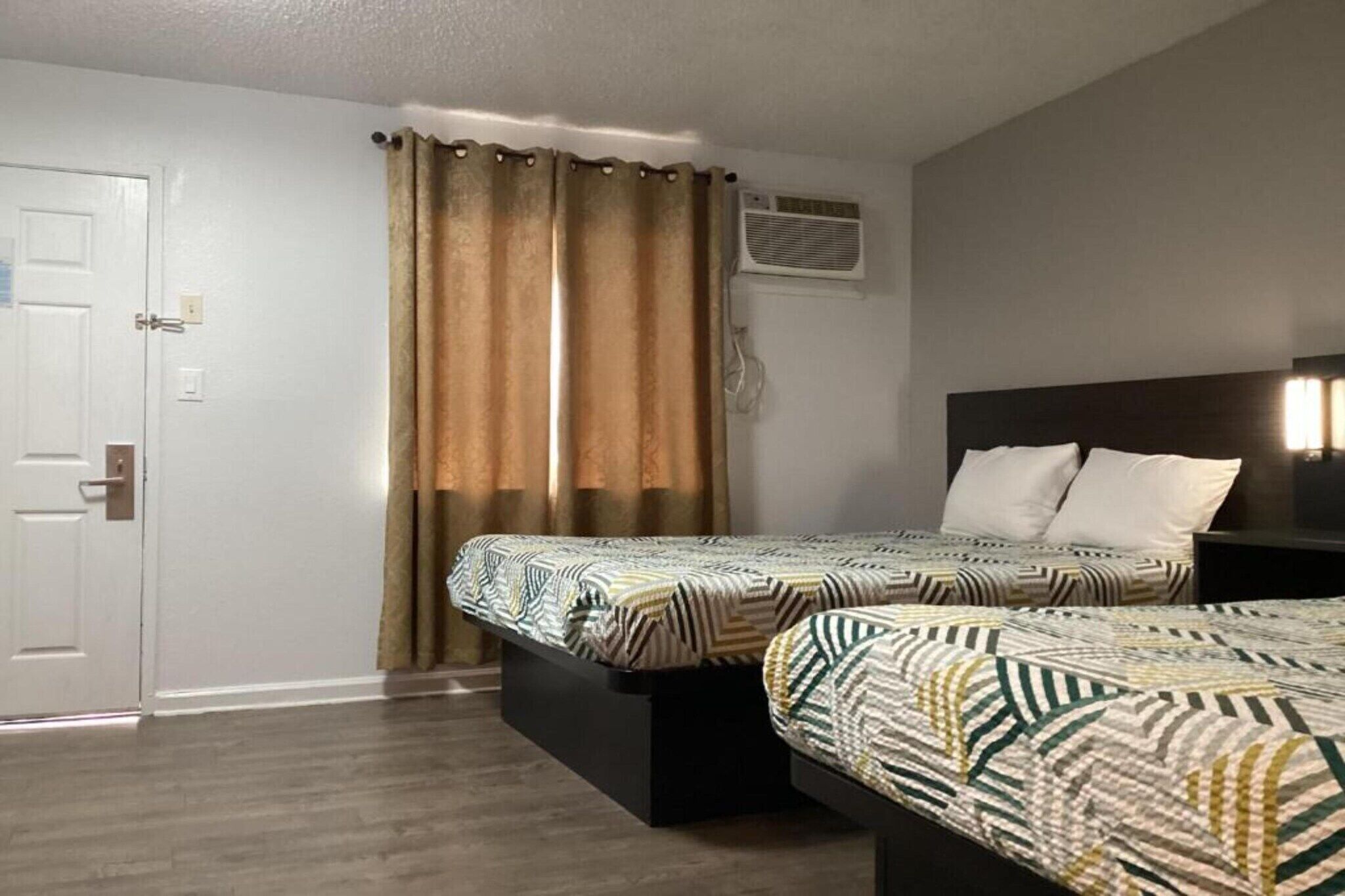 Une chambre avec deux lits, une porte, un appareil de climatisation et un rideau.