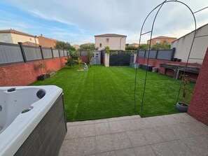 A backyard with a hot tub, a well-maintained lawn, a small shed, and a metal arch structure.