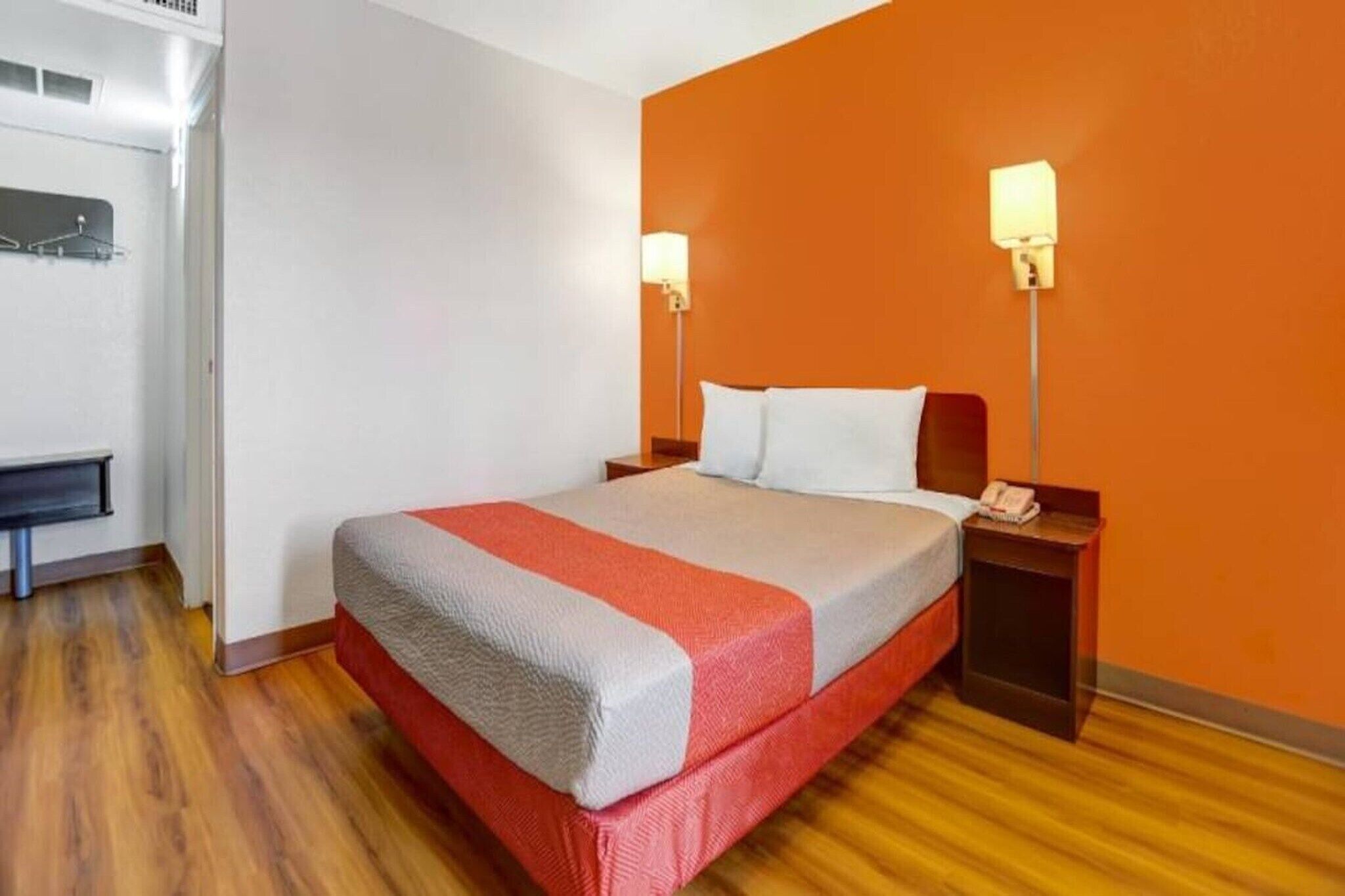 Una habitación de hotel con una cama, dos lámparas de noche, una mesita de noche y suelo de madera.