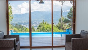 Ein Zimmer mit einer großen Schiebeglaswand, die zu einem Pool führt, mit Korbmöbeln und Bergblick.