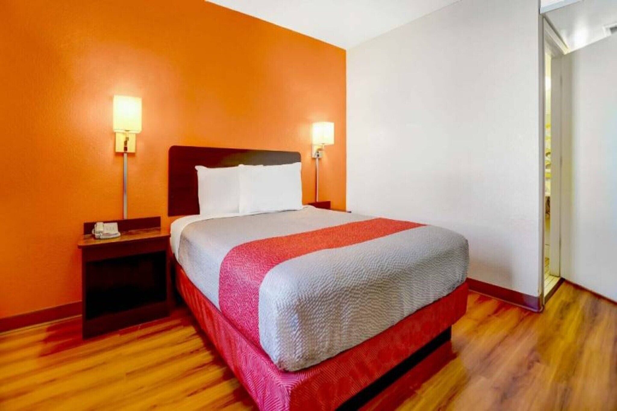 A hotel room with a bed, two bedside lamps, a nightstand, and a wooden floor.
