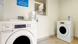 A laundry area with two Whirlpool washers, a sign indicating the motel is not responsible for unattended items, and a window with a view. - 1 King Bed | Non-Smoking (Grants)