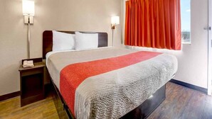 Une chambre d’hôtel avec un lit, une table de chevet et deux lampes fixées au mur.