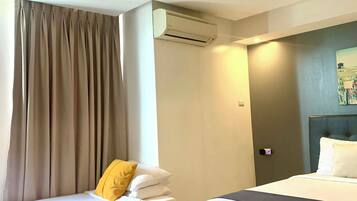 A hotel room with two beds, an air conditioning unit, a headboard with a light fixture, and a window with curtains.