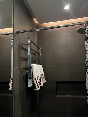 A modern bathroom with a glass shower enclosure, a towel rack, and a patterned shower curtain. - The Upperhouse Hotel (Cagayan de Oro)