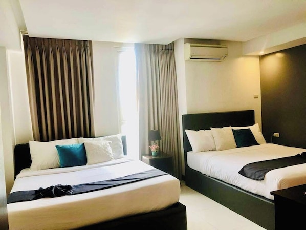A hotel room with two beds, a bedside table, an air conditioning unit, and a window with curtains. - The Upperhouse Hotel (Cagayan de Oro)