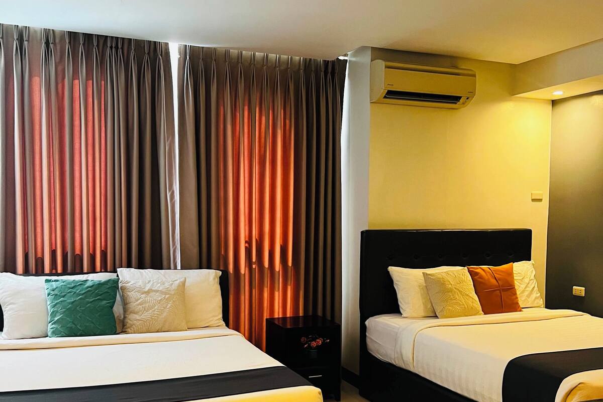 A hotel room with two beds, a nightstand, an air conditioning unit, and a curtain.