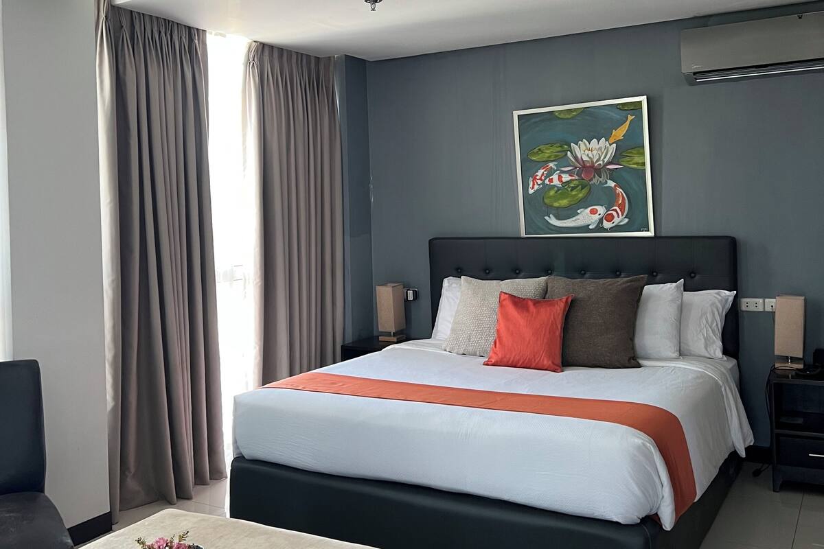 A modern hotel room with a large bed, a bedside table, a chair, and a painting on the wall.