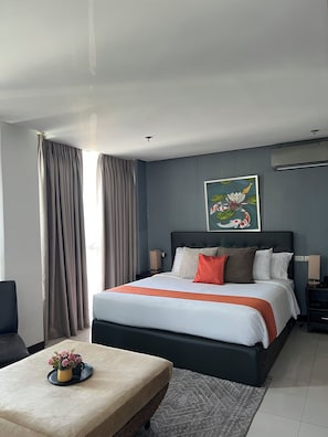 Moderni hotellihuone, jossa on suuri sänky, yöpöytä, tuoli ja taulu seinällä.