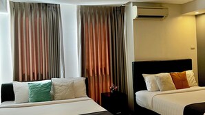 A hotel room with two beds, a bedside table, an air conditioning unit, and curtains. - The Upperhouse Hotel Boutique Stay with City & River Views (Cagayan de Oro)