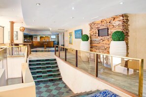 Un vestíbulo de hotel con una escalera, una recepción y una pared de piedra con macetas decorativas.
