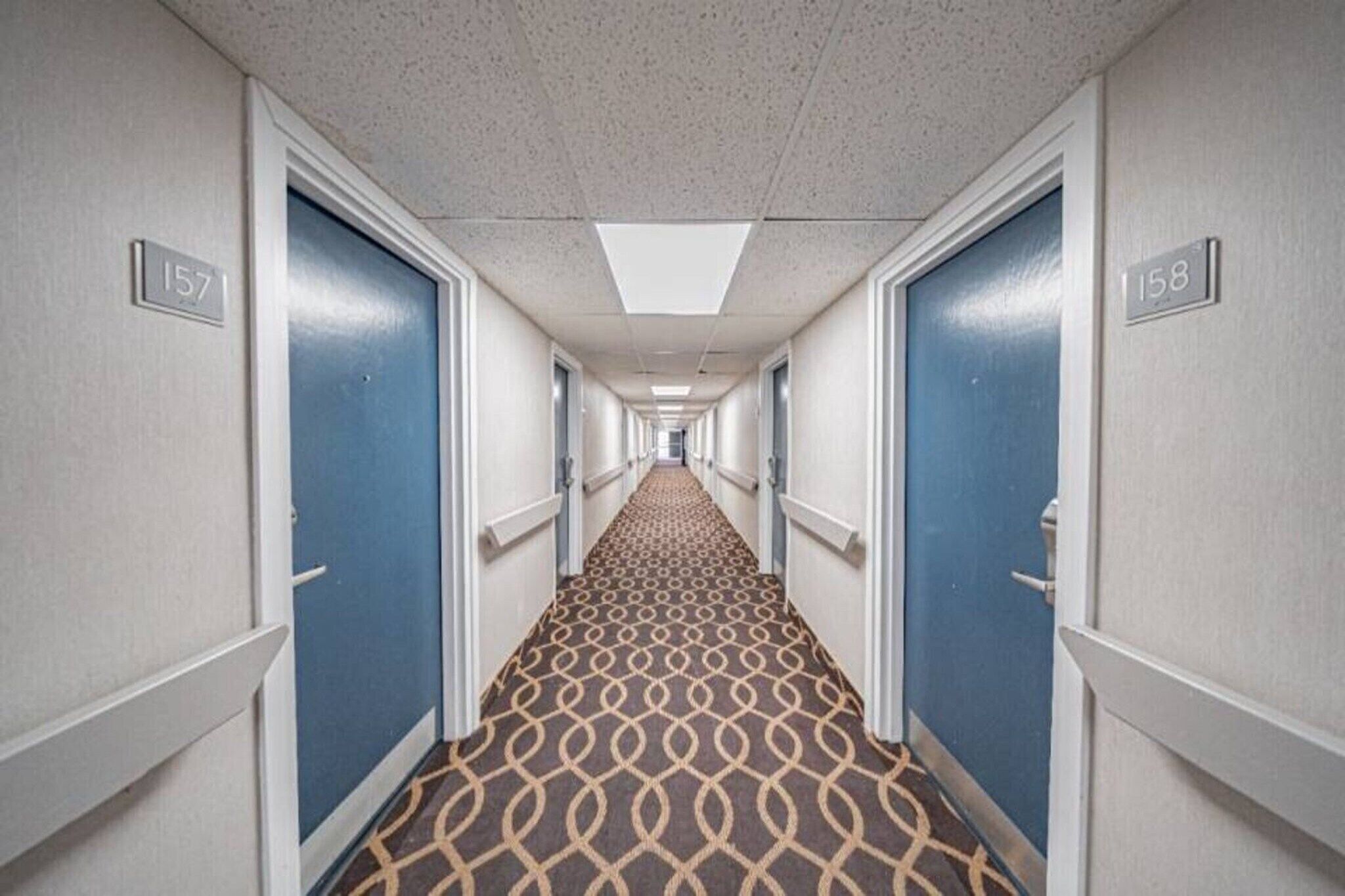 A hotel hallway with blue doors, numbered 157 and 158, and a patterned carpet.