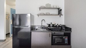 Cocina compacta con refrigerador de acero inoxidable, microondas, pileta y una estantería con vajilla.