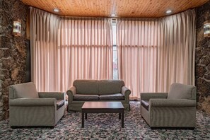 A room with a wooden ceiling, a stone wall, a beige sofa, two armchairs, and a patterned carpet.